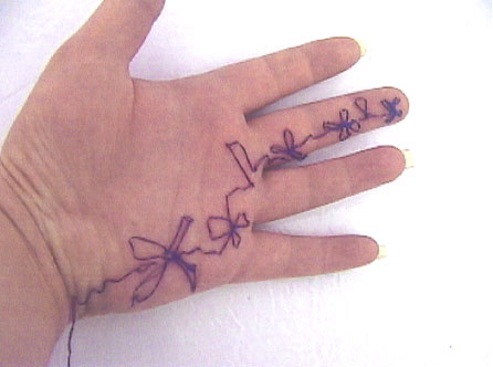 A video still from Christina Mancuso's Untitled (Performance #4), a hand with purple thread sewn onto the skin, from the bottom of the wrist, along the palm to the middle finger, with arough pattern of flowers