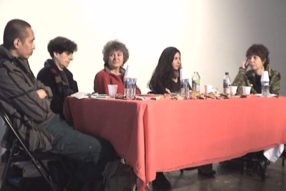 Panelists Mideo M. Cruz, Esther Ferrer, Cheryl L'Hirondelle, Glenda León and moderator Johanna Householder sit at a table conversing as part of the panel "Infiltration" (2004)