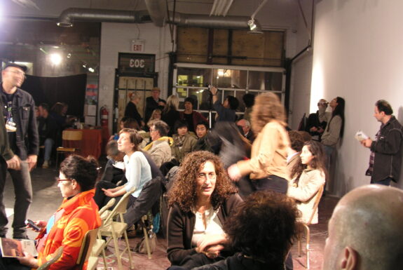 A candid photograph of the audience at XPACE chatting between performances at the 2004 7a*11d festival