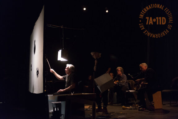Hank Bull performing The Red Jewell, Another Thrilling Episode in the Timeless Saga, Donkey Tales, as Told in Shadow Play by Hank Bull, with Live Music by Bob Vespaziani and Arthur Bull at the Theatre Centre