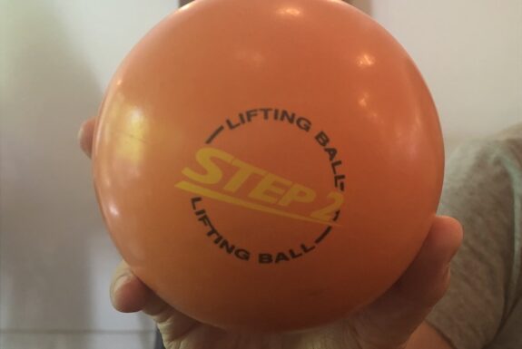 A hand holds up an orange ball with the words 'Step 2' printed on it.