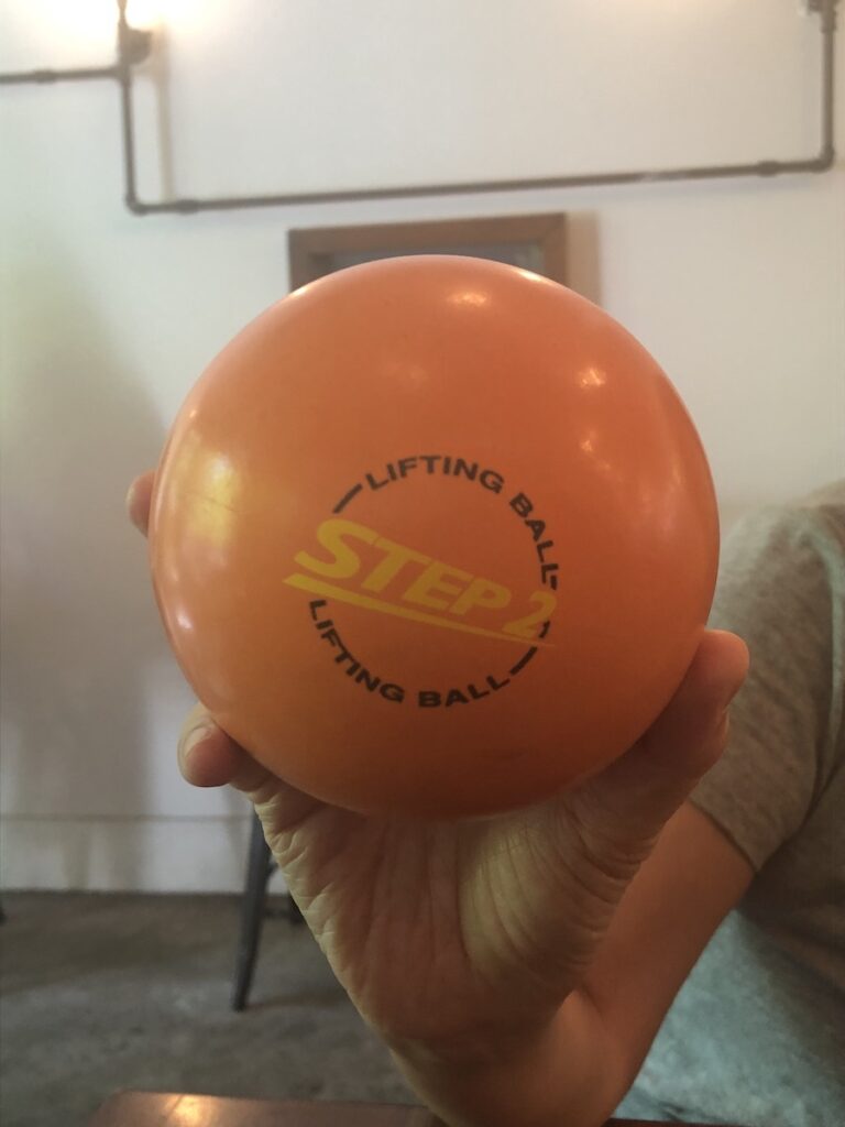 A hand holds up an orange ball with the words 'Step 2' printed on it.