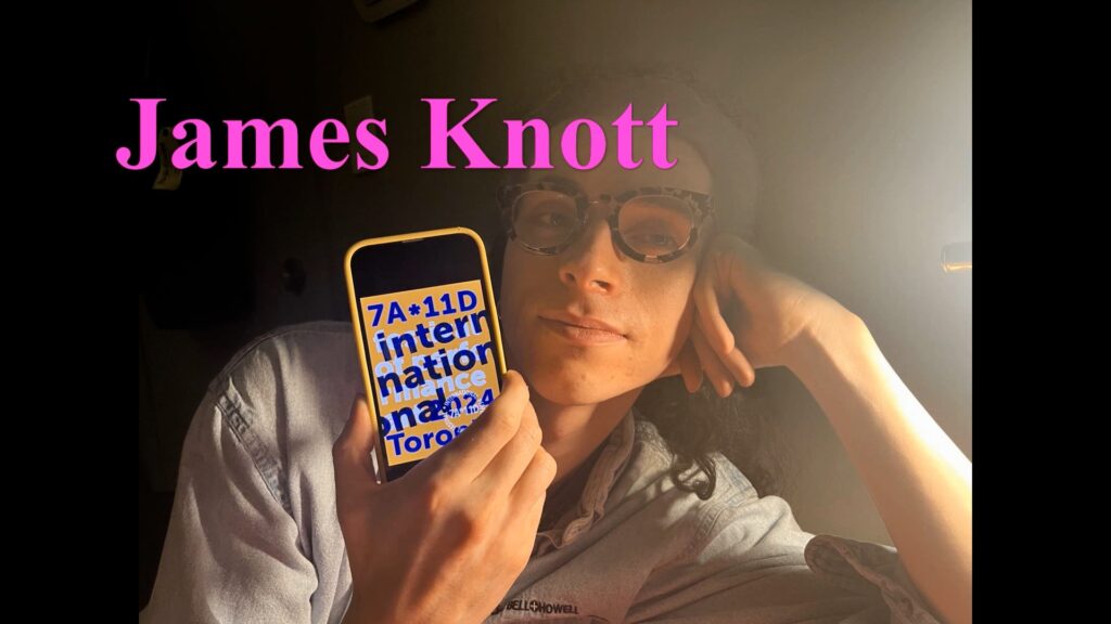 In this screen shot from Margaret Dragu's Typical Day: James Knott illustrated audio podcast, a person wearing tortoise shell glasses faces the camera. The name James Knott appears in pink letters across the upper part of the screen. James's head is propped against one arm. In their other hand, they hold a cellphone, face turned toward the camera, with the 2024 7a*11d International Festival of Performance Art logo displayed.