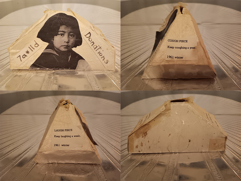 4 images — front side and back views — of a "donation box" made from off-white handmade paper. The box is pyramid-shaped, with a slot at the top for receiving money. The front side features a black-and-white photocopy image of Yoko Ono as a child, with additional small sheets of paper affixed o either side with words written in black marker. One says "7a*11d", and the other, "Donations". One side view features a photocopied instruction piece from Yoko Ono's Grapefruit. "COUGH PIECE. Keep coughing a year. 1961 winter." The backside is unadorned, though small patches of brown dot the surface of the paper, which has yellowed with age, and yellowed areas of scotch tape used in the assembly are also visible. The other side panel also features a photocopied instruction piece from Yoko Ono's Grapefruit. "LAUGH PIECE. Keep laughing a week. 1961 winter".